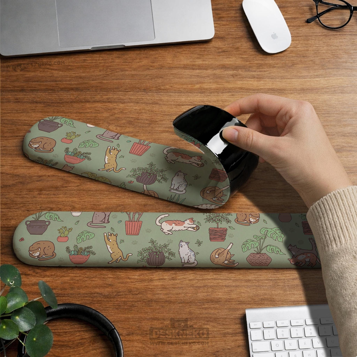 Sage green desk mat with a pattern of lounging cats, leafy plants, cactus pots, and earthy botanical details.