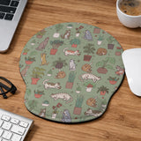 Sage green desk mat with a pattern of lounging cats, leafy plants, cactus pots, and earthy botanical details.