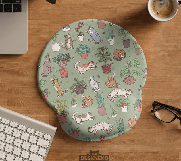 Sage green desk mat with a pattern of lounging cats, leafy plants, cactus pots, and earthy botanical details.