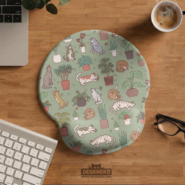 Sage green desk mat with a pattern of lounging cats, leafy plants, cactus pots, and earthy botanical details.