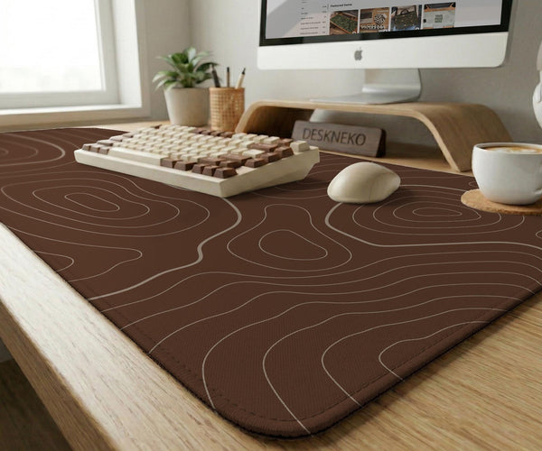 Brown desk mat with a repeating topographic contour line pattern in a neutral earth tone design.