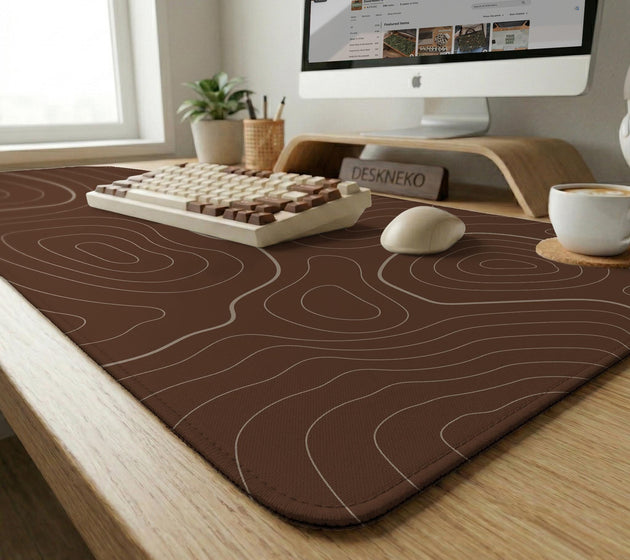 Brown desk mat with a repeating topographic contour line pattern in a neutral earth tone design.