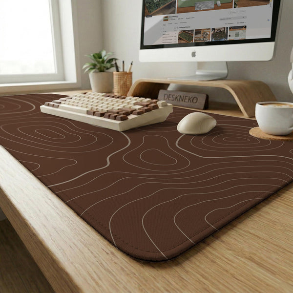 Brown desk mat with a repeating topographic contour line pattern in a neutral earth tone design.