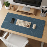 A slate blue desk mat with thin contour line map art on a light background.
