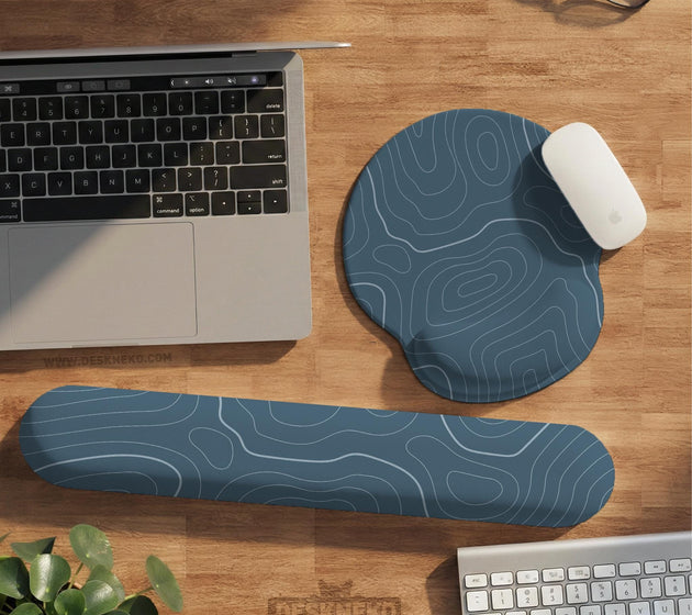 Muted blue desk mat with thin topographic line art pattern shown with matching mousepad and keyboard wrist rest options.
