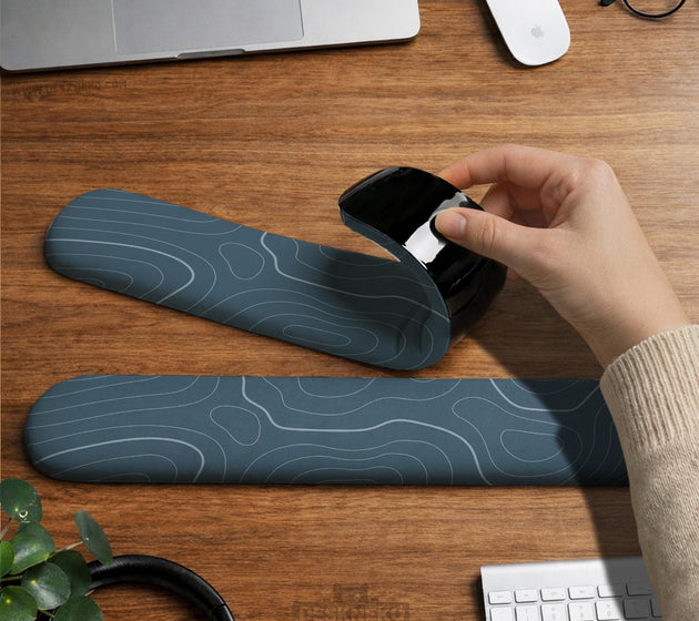 Muted blue desk mat with thin topographic line art pattern shown with matching mousepad and keyboard wrist rest options.