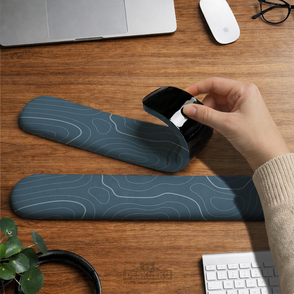 Muted blue desk mat with thin topographic line art pattern shown with matching mousepad and keyboard wrist rest options.