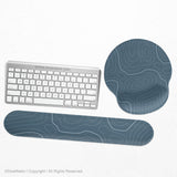 Muted blue desk mat with thin topographic line art pattern shown with matching mousepad and keyboard wrist rest options.