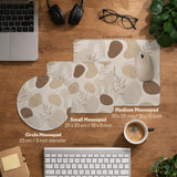 Beige desk mat with fine botanical line drawings and soft abstract shapes on a light neutral background.