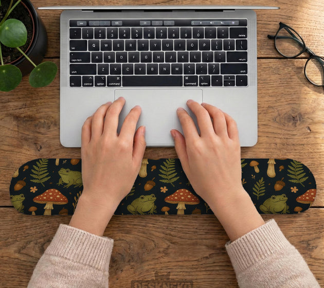 Dark botanical desk mat options with frogs, mushrooms, ferns, and acorns in brown and green tones, plus a matching keyboard wrist rest.