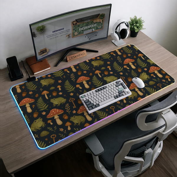 Dark forest-themed desk mat with an all-over pattern of frogs, mushrooms, fern leaves, acorns, tiny flowers, and antique keys.