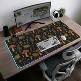 Dark forest-themed desk mat with an all-over pattern of frogs, mushrooms, fern leaves, acorns, tiny flowers, and antique keys.