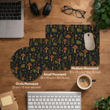 Dark forest-themed desk mat with an all-over pattern of frogs, mushrooms, fern leaves, acorns, tiny flowers, and antique keys.