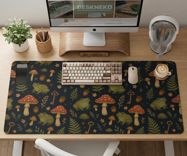 Dark forest-themed desk mat with an all-over pattern of frogs, mushrooms, fern leaves, acorns, tiny flowers, and antique keys.