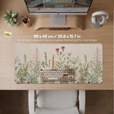 A desk mat with a botanical meadow design featuring wildflowers, leafy stems, and soft neutral colors.