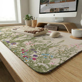 A desk mat with a botanical meadow design featuring wildflowers, leafy stems, and soft neutral colors.