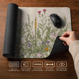 A desk mat with a botanical meadow design featuring wildflowers, leafy stems, and soft neutral colors.