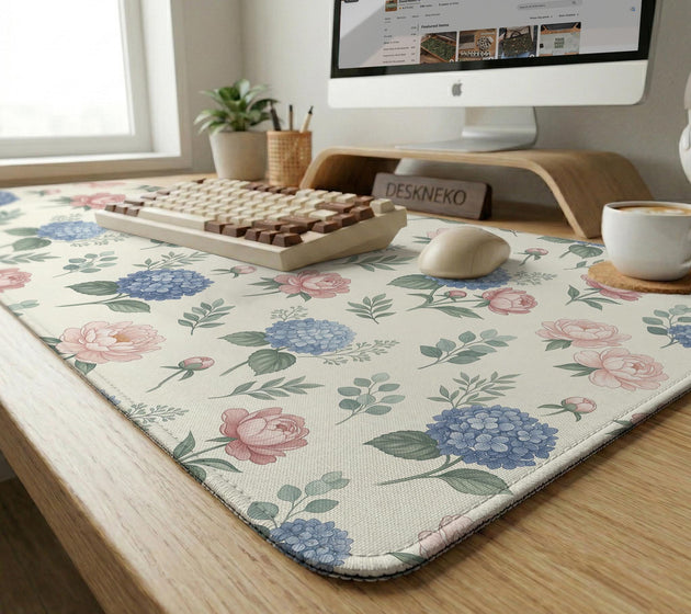 Floral desk mat with sage greenery, pink peonies, blue flowers, and a warm cream background.