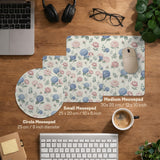 Floral desk mat with sage greenery, pink peonies, blue flowers, and a warm cream background.