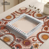 A square mahjong mat with a scalloped edge, sun and moon artwork, terracotta flowers, a soft cream background, and a decorative border around the play area.