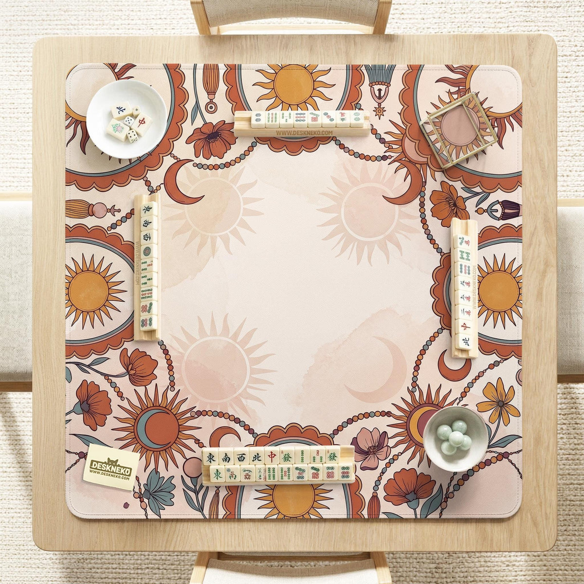 A square mahjong mat with a scalloped edge, sun and moon artwork, terracotta flowers, a soft cream background, and a decorative border around the play area.
