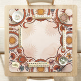 A square mahjong mat with a scalloped edge, sun and moon artwork, terracotta flowers, a soft cream background, and a decorative border around the play area.