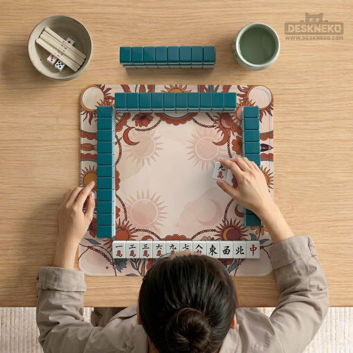 A square mahjong mat with a scalloped edge, sun and moon artwork, terracotta flowers, a soft cream background, and a decorative border around the play area.