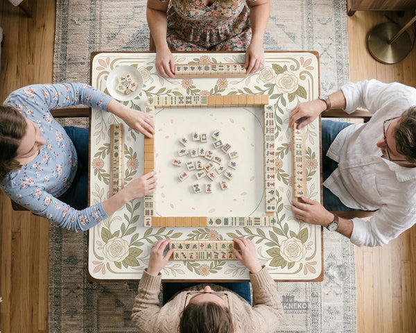 Square mahjong mat with a light floral border in sage green, cream, and blush around a plain center play area.
