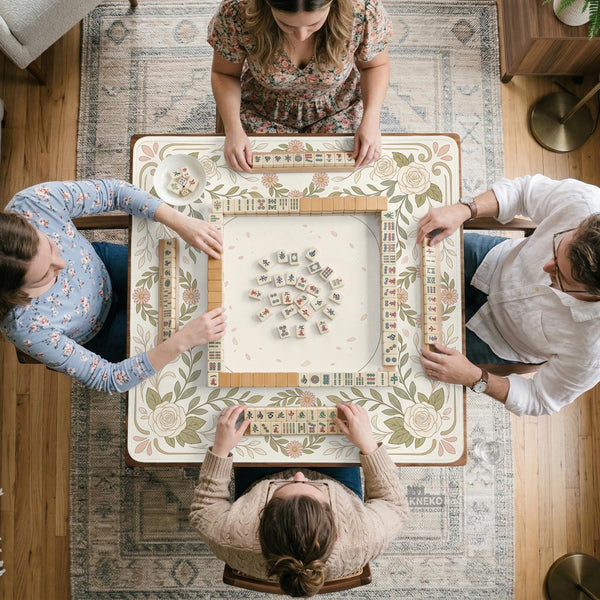 Square mahjong mat with a light floral border in sage green, cream, and blush around a plain center play area.