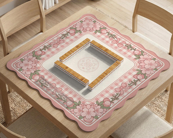 Square pink mahjong mat with a gingham border, floral corner details, and ribbon accents on a light background.