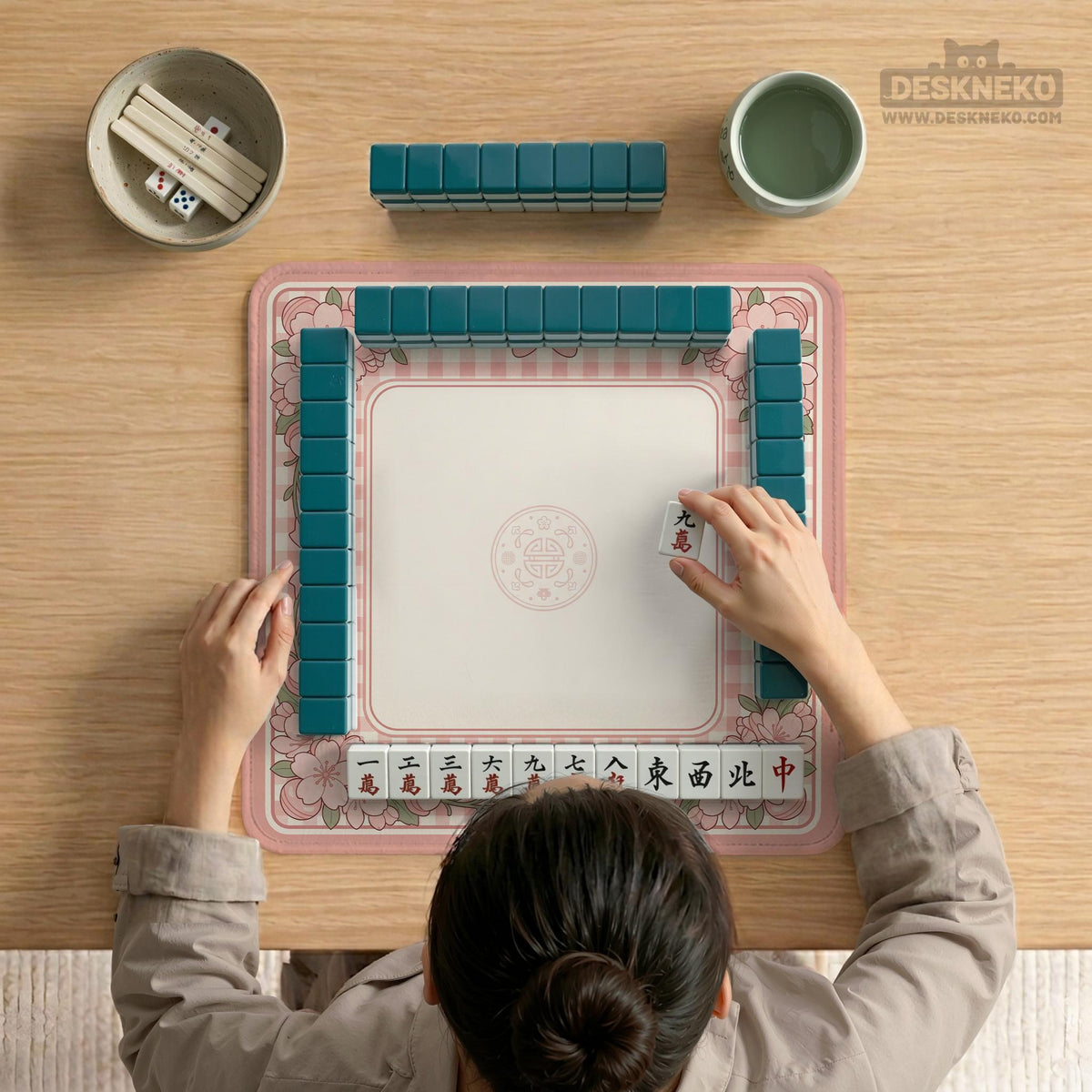 Square pink mahjong mat with a gingham border, floral corner details, and ribbon accents on a light background.