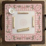 Pink gingham mahjong mat with a floral border, cherry blossom details, and a bow design around a plain center play area.