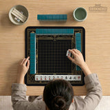 Black and gold square mahjong mat with a scalloped edge, geometric border, thin line details, fan motifs, and dragon and phoenix accents around an open center.