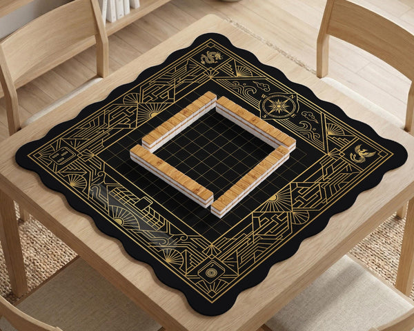 Black and gold square mahjong mat with a scalloped edge, geometric border, thin line details, fan motifs, and dragon and phoenix accents around an open center.