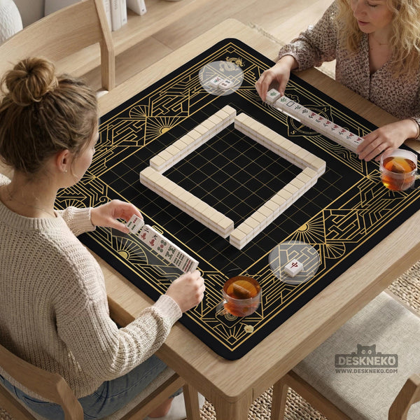 Black and gold square mahjong mat with a scalloped edge, geometric border, thin line details, fan motifs, and dragon and phoenix accents around an open center.