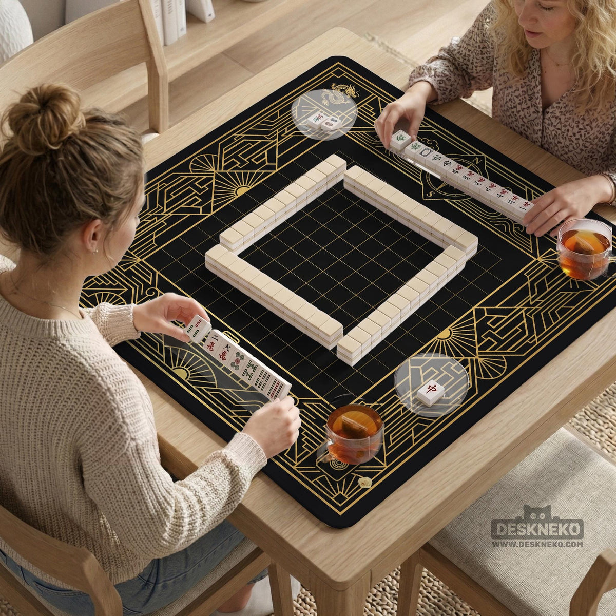 Black and gold square mahjong mat with a scalloped edge, geometric border, thin line details, fan motifs, and dragon and phoenix accents around an open center.