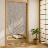 Beige door curtain with a crescent moon, leafy botanical branches, gray line art, and dotted celestial details.