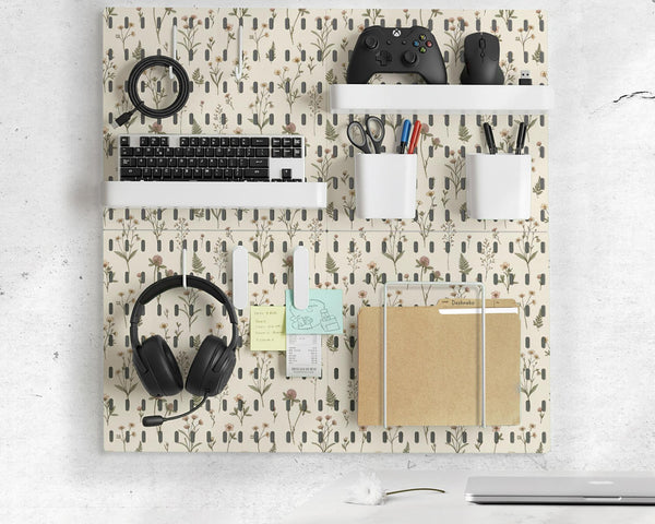 Cream pegboard wall organizer with small floral print, sage green stems, black slot layout, shelves, hooks, clips, and containers.
