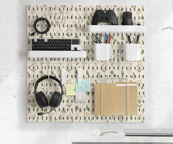 Cream pegboard wall organizer with small floral print, sage green stems, black slot layout, shelves, hooks, clips, and containers.