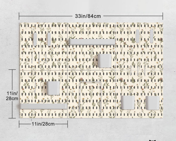Cream pegboard wall organizer with small floral print, sage green stems, black slot layout, shelves, hooks, clips, and containers.