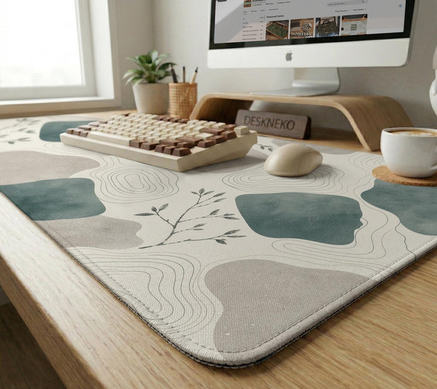A desk mat with sage green abstract blocks, cream space, gray stone-like shapes, fine topographic contour lines, and small branch details.