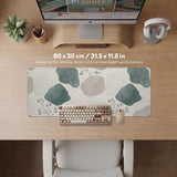 A desk mat with sage green abstract blocks, cream space, gray stone-like shapes, fine topographic contour lines, and small branch details.