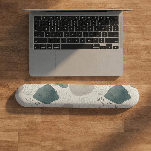 Sage green ergonomic mousepad and keyboard wrist rest with abstract shapes, soft gray details, cream space, topographic contour lines, and leafy branch accents.