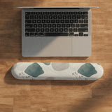 Sage green ergonomic mousepad and keyboard wrist rest with abstract shapes, soft gray details, cream space, topographic contour lines, and leafy branch accents.