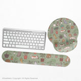 Sage green desk mat with a pattern of lounging cats, leafy plants, cactus pots, and earthy botanical details.