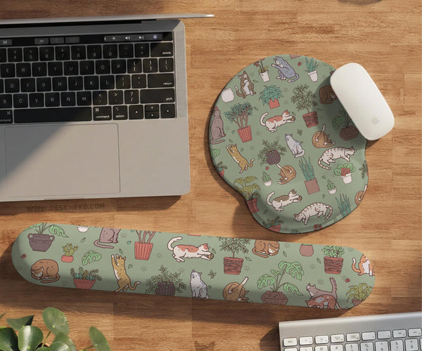 Sage green desk mat with a pattern of lounging cats, leafy plants, cactus pots, and earthy botanical details.
