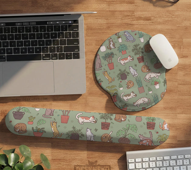 Sage green desk mat with a pattern of lounging cats, leafy plants, cactus pots, and earthy botanical details.