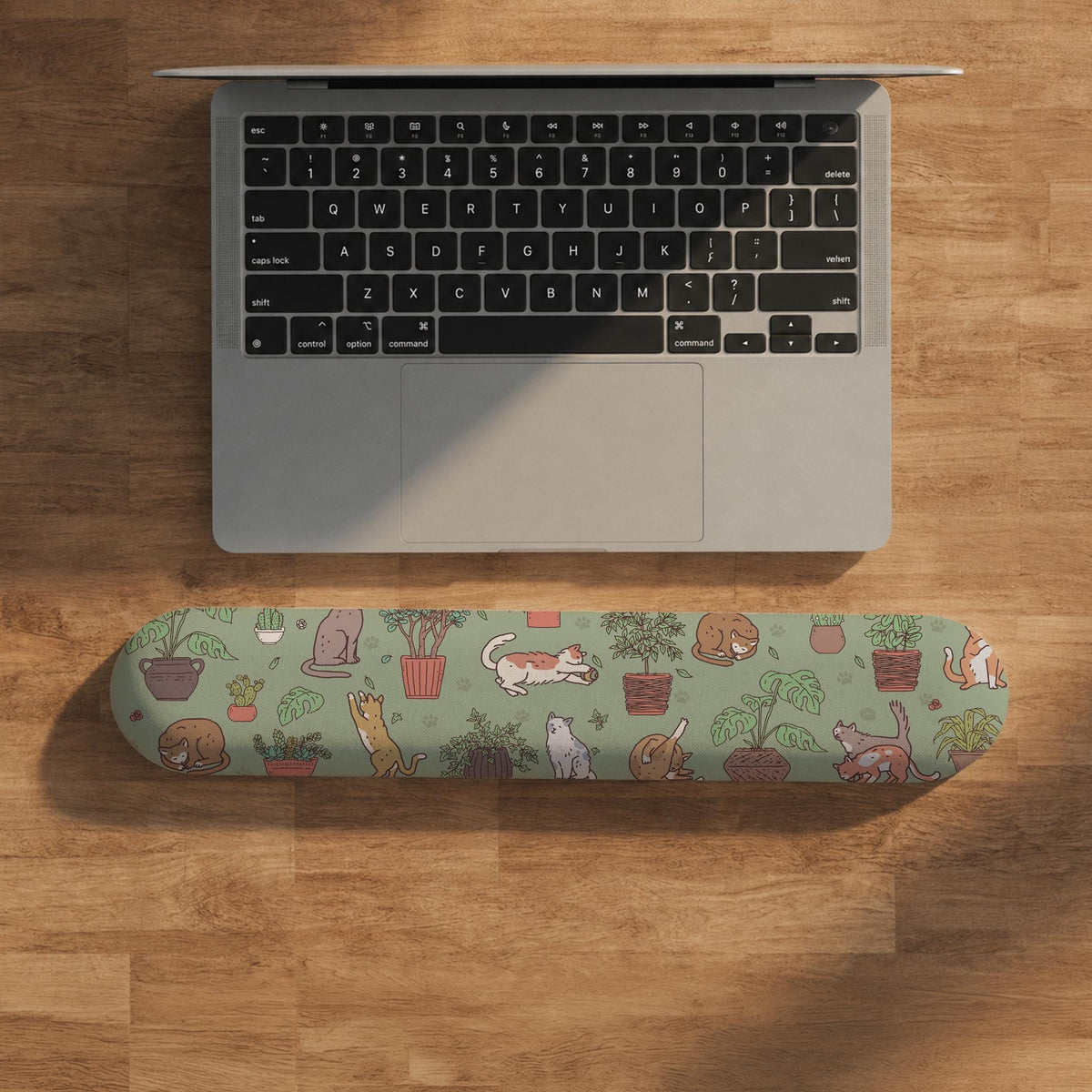 Sage green desk mat with a pattern of lounging cats, leafy plants, cactus pots, and earthy botanical details.