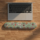 Sage green desk mat with a pattern of lounging cats, leafy plants, cactus pots, and earthy botanical details.