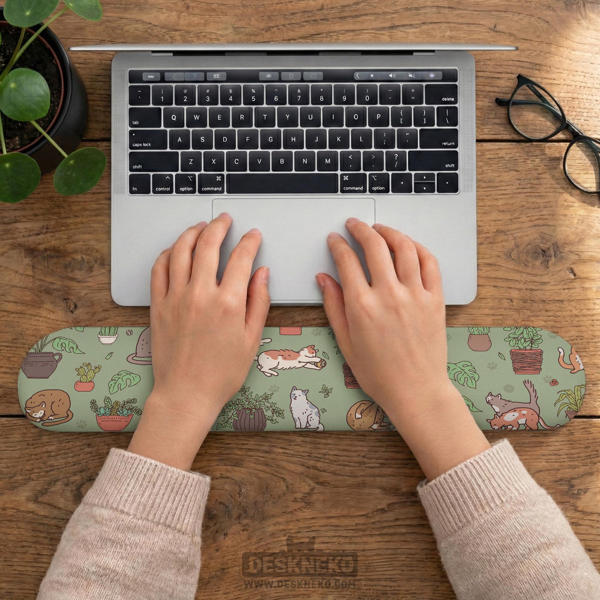 Sage green desk mat with a pattern of lounging cats, leafy plants, cactus pots, and earthy botanical details.